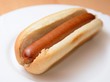 A cooked hot dog in a plain soft bun on a white plate.