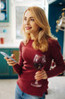 © zinkevych - Inspired. Pretty alert blond young woman smiling and holding a phone while drinking some red wine and thinking