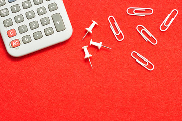 A calculator, pushpins and paperclips displayed on a red background