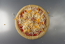 Top View Of A Pizza Crust With Tomato Sauce And A Blend Of Cheeses On A Metal Baking Pan.