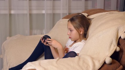 young girl sitting in comfortable chair and looking at screen mobile phone