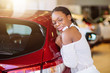 © alfa27 - Smiling african woman hugging a red car at new car showroom