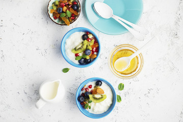 Wall Mural - Breakfast, rice porridge or natural yoghurt with assorted berries, fruits and nuts: kiwi, pomegranate, blueberries, almonds, dried apricots in small bowls on a light background. Top view. Copy space.