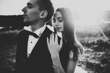 Happy newlywed couple posing and smiling in wedding dress and suit outdoor, black and white