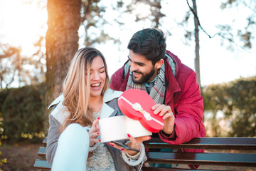 Wall Mural - Young woman receiving a surprise gift red box from her boyfriend on wood chair.