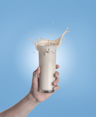 Sticker - Hand holding glass of milk with a splash on a blue background