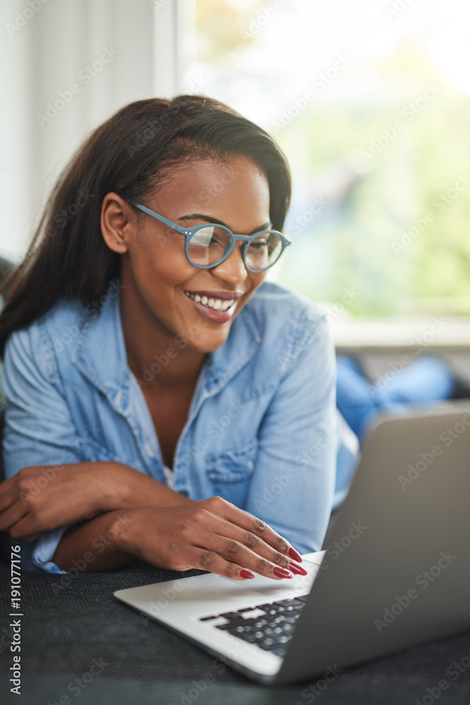 Smiling African woman relaxing on her sofa using a laptop Stock Photo ...