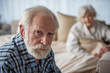 © Yakobchuk Olena - Portrait of depressed old pensioner looking at camera with upset look. Focus on his face. His wife is sitting in bed on background