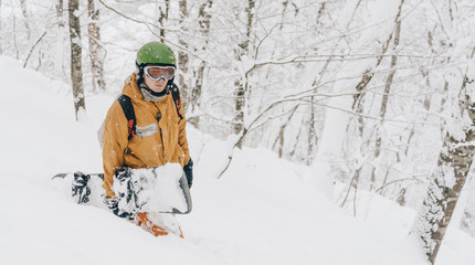 Sporty guy walking with snowboard in forest after snowfall.