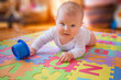 Cute baby in white vest, reaching for cups while on lying on tummy on alphabet mat.