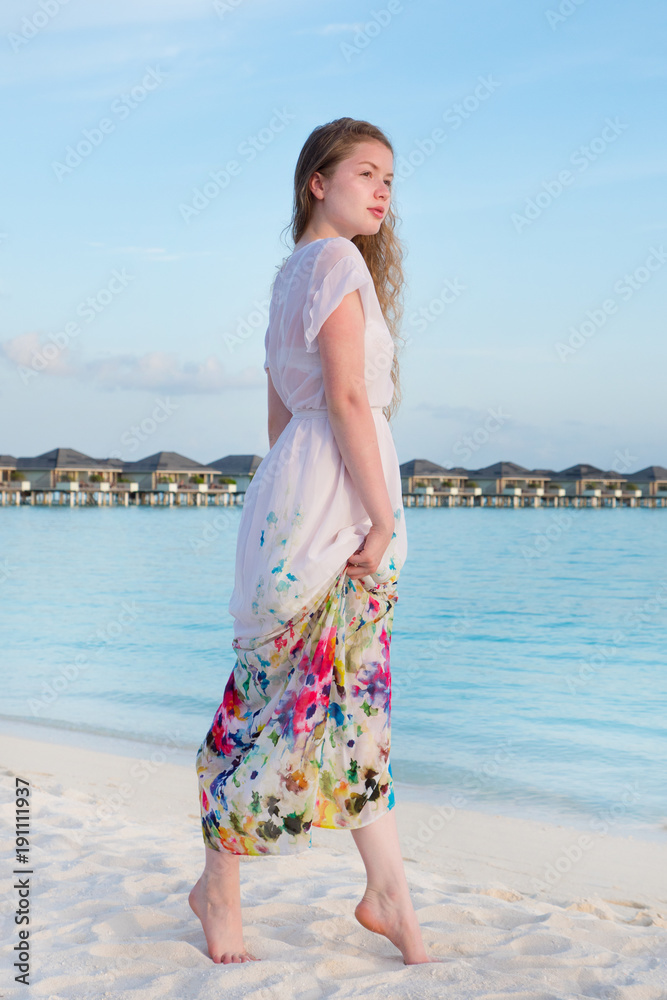 Photo Stock Young beautiful woman in dress on the seashore Maldives.  Beautiful and fashion woman with long legs in white dress, posing on the  tropical beach. Girl on a beach in white