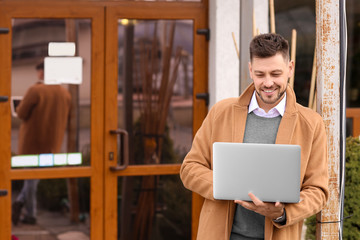 Business owner holding laptop near his store, outdoors