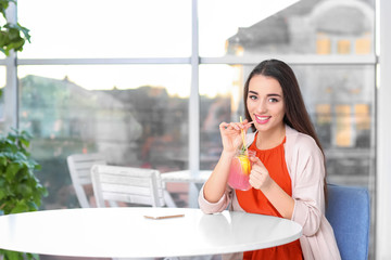 Wall Mural - Young woman with mason jar of pink lemonade in cafe