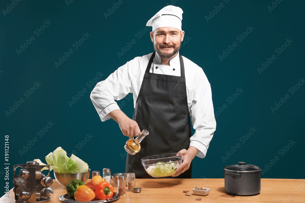 Handsome male chef adding oil to salad at table against color background