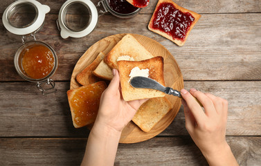 Wall Mural - Woman spreading butter on toasted bread over table, top view