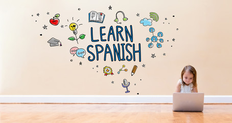 Wall Mural - Learn Spanish text with little girl using a laptop computer on floor