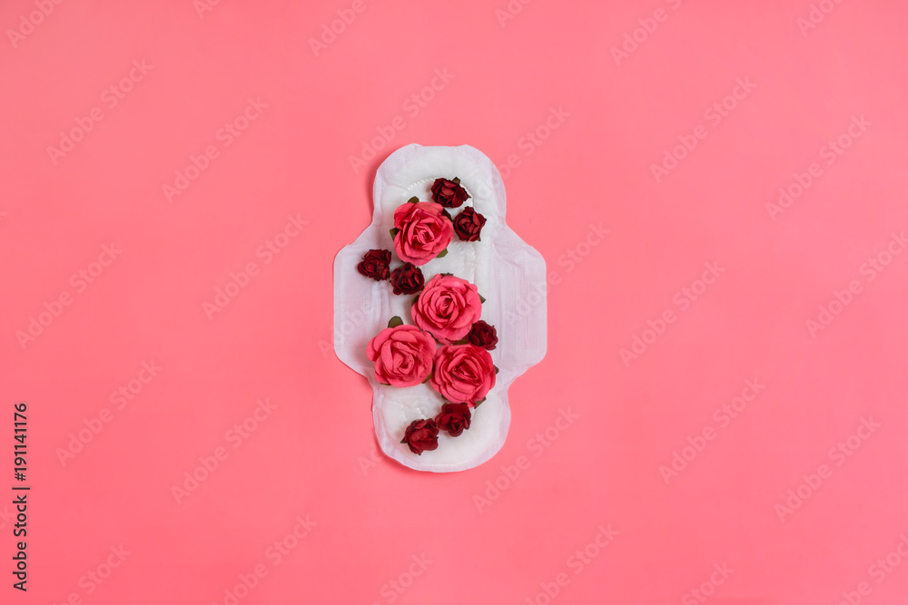 White sanitary pad with red and pink flowers on it, woman health or body positive concept. Pink background.  Flatlay. Copyspace - obrazy, fototapety, plakaty 