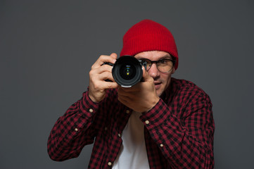 Wall Mural - Positive blurred hipster man in stylish clothes photographer holds camera and takes photo on background in violet color tone