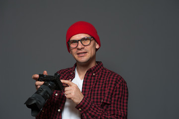 Wall Mural - Stylish young man photographer holding camera in his hands and posing on gray background