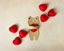 Congratulations On The Valentine's Day. A Small Bear Of Kraft Paper Holds In His Paws A Chocolate Candy In The Form Of A Heart In A Red Foil