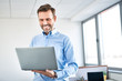© baranq - Happy business worker standing in office with laptop