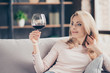 © deagreez - Portrait of pretty, charming, attractive, stylish connoisseur woman sitting on couch having raised glass with red wine in hand, examine, taste beverage