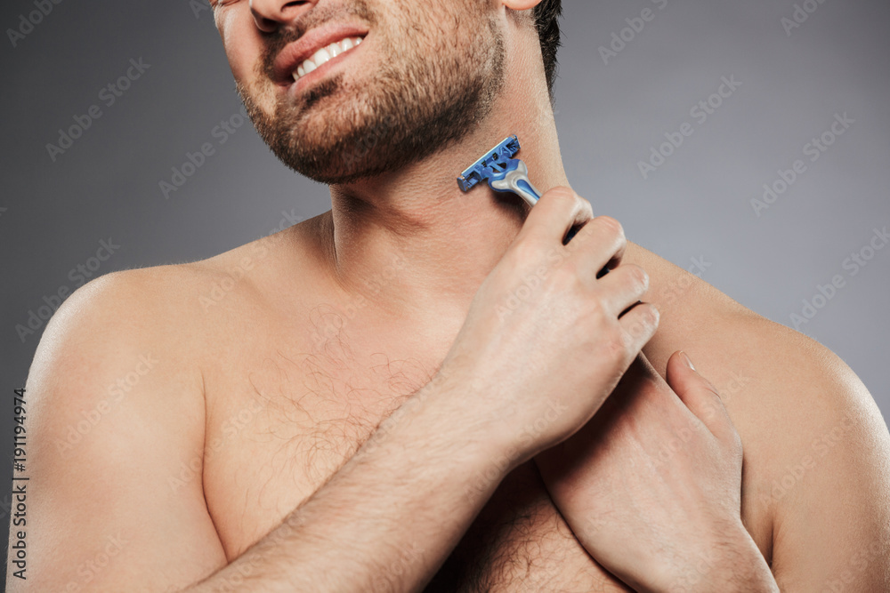 Cropped picture of naked man smiling and shaving his neck with razor