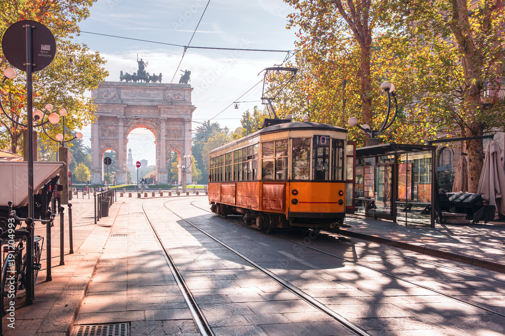 Famous vintage tram in the centre of the Old Town of Milan in the sunny day, Lombardia, Italy. Arch of Peace, or Arco della Pace on the background. - obrazy, fototapety, plakaty 