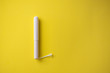Feminine tampon with paper applicator on yellow background