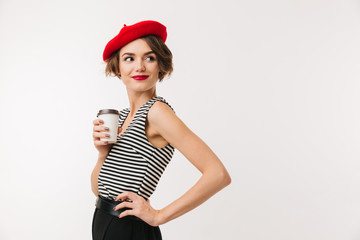 Canvas Print - Attractive woman having french style wearing red beret posing on camera with takeaway coffee in paper cup and looking aside, isolated over white wall