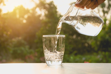 Person pouring water from pitcher to glass on nature background