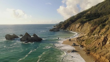 aerial shot flying over a pristine sandy beach on a rugged coastline. very colorful and epic views. 