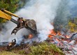 Backhoe bucket pushing in branches and stumps in burn pile