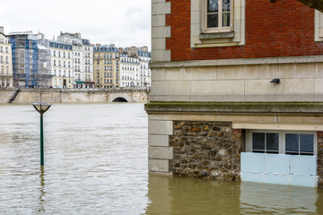 View of a brick house on the wharf of the Seine in Paris, half-submerged by the water during the flood episode of January 2018, with period buildings of the Saint-Louis island in the background.