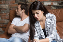 Sad Pensive Young Girl Thinking Of Relationships Problems Sitting On Sofa With Offended Boyfriend, Conflicts In Marriage, Upset Couple After Fight Dispute, Making Decision Of Breaking Up Get Divorced