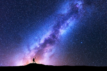 Wall Mural - silhouette of happy woman with trekking poles against purple milky way at night. space background. l