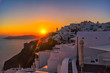 Die Sonne geht über den weißen Häusern von Santorin unter, man erkennt die abschüssige Lage der griechischen Trauminsel