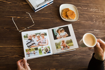 the Hand senior woman holding a family photo album against the background of the a wooden table.