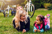 Happy Mother And Daughter Lying Outdoors Smiling And Hugging Bicycles