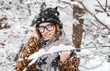 © proimagecontent - Young girl wears warm hat, scarf and glasses near snowy branches of tree in the park, outdoor sunny day