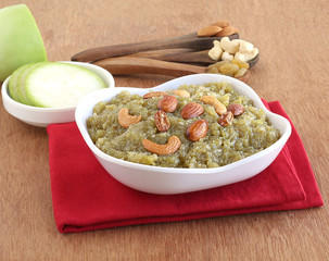 Wall Mural - Lauki halwa, also known as doodhi, ghiya, or bottle gourd halwa, is a traditional and popular Indian sweet dish, on a wooden background with some of its main ingredients.