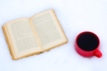 Red cup of coffee or tea with a red book or notebook or photo albums with heart. Snow is coming. Winter concept of Valentine's Day