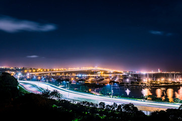 cars in motion on a lighted bridge and highway over the sea with anchored sailing boats in a marina of Auckland in New Zealand with a Starry sky