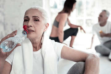 Wall Mural - Don t forget about water. Pensive retired lady taking a break and drinking her water after taking part in an intense training session.