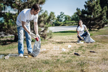 Poster - Eco project. Happy positive nice man holding a plastic bag and cleaning rubbish while participating in eco project