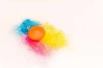 one chicken egg on a background of bright blue and yellow colours on a white background. colored powder. easter concept.