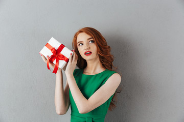 Wall Mural - Thinking redhead young woman in green dress holding surprise