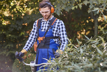 Wall Mural - Gardener with goggles and headphones using weedwacker