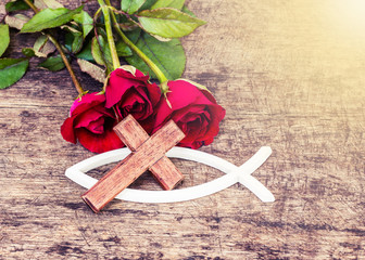 Wall Mural - The white christian fish and  wooden cross shows  christian symbol with red roses flowers on old wooden background, copy space, vintage tone effect