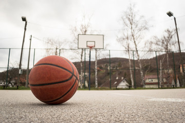 Used orange basketball with basket in background. Basketball street court